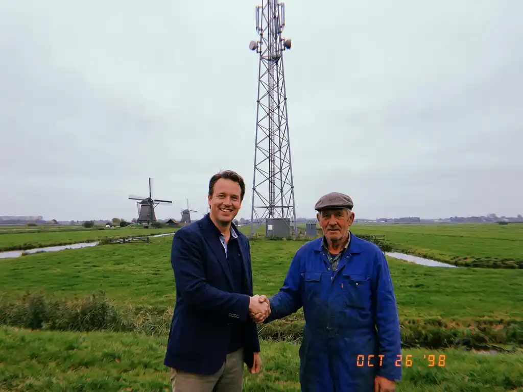 Nederlandse zakenman en boer schudden handen voor telecommunicatietoren met windmolens op achtergrond